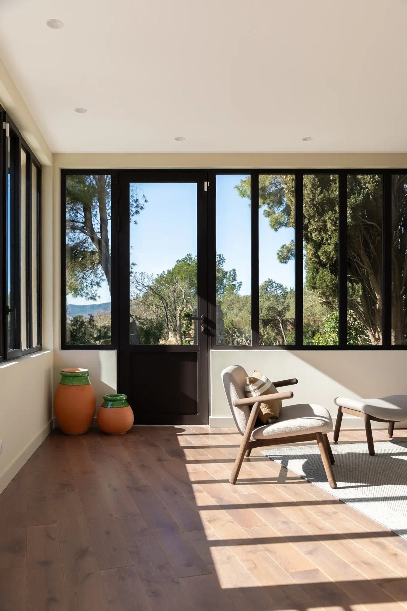 extension de maison véranda avec verrière style atelier bibliothèque métal AMPM canapé et fauteuils Bolia sol en parquet foncé