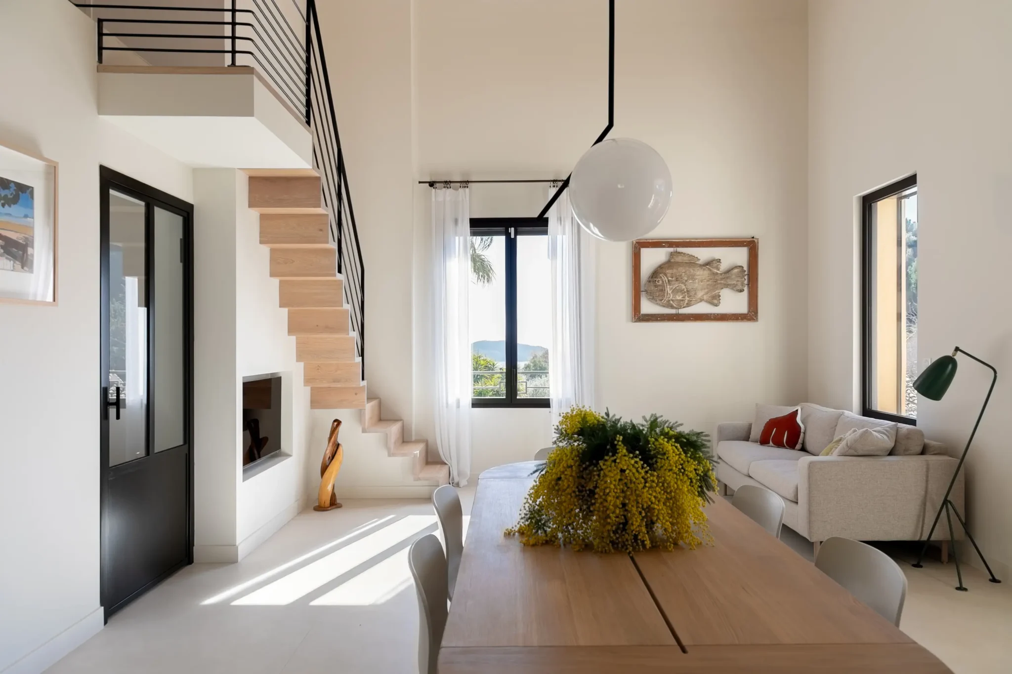 alle à manger avec table de chez Bolia porte vitrée sur mesure en fer forgé escalier gain de place avec main courante en métal noir carrelage sol grand format effet béton ciré salon avec télé encastré dans mur
