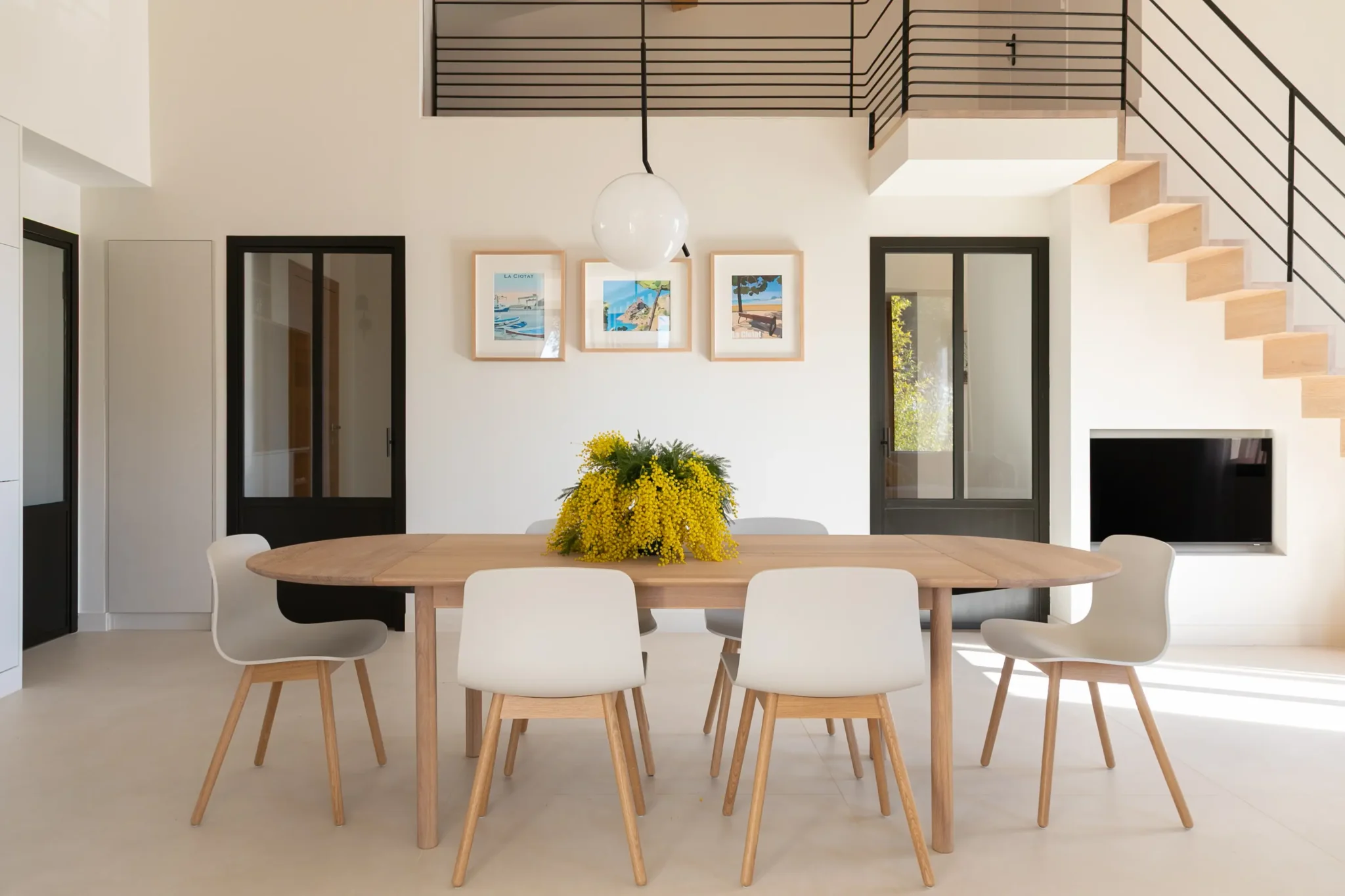 salle à manger avec table de chez Bolia porte vitrée sur mesure en fer forgé escalier gain de place avec main courante en métal noir carrelage sol grand format effet béton ciré