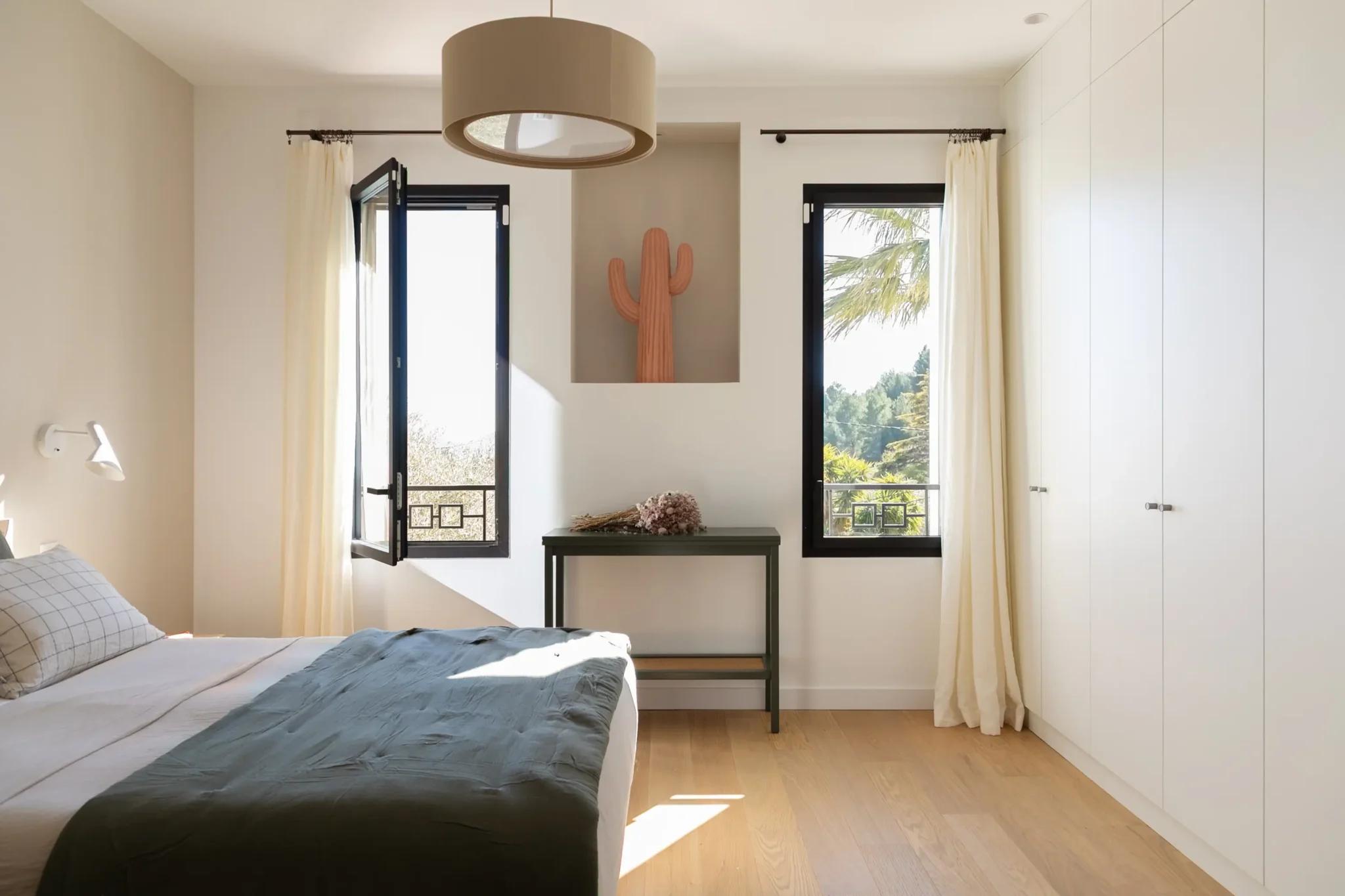 chambre avec sol en parquet rideaux en lin tête de lit en rotin et tapis rond décoration chambre draps de lit vert en lin grand placard dressing sur mesure fenêtre vue mer niche murale avec décoration