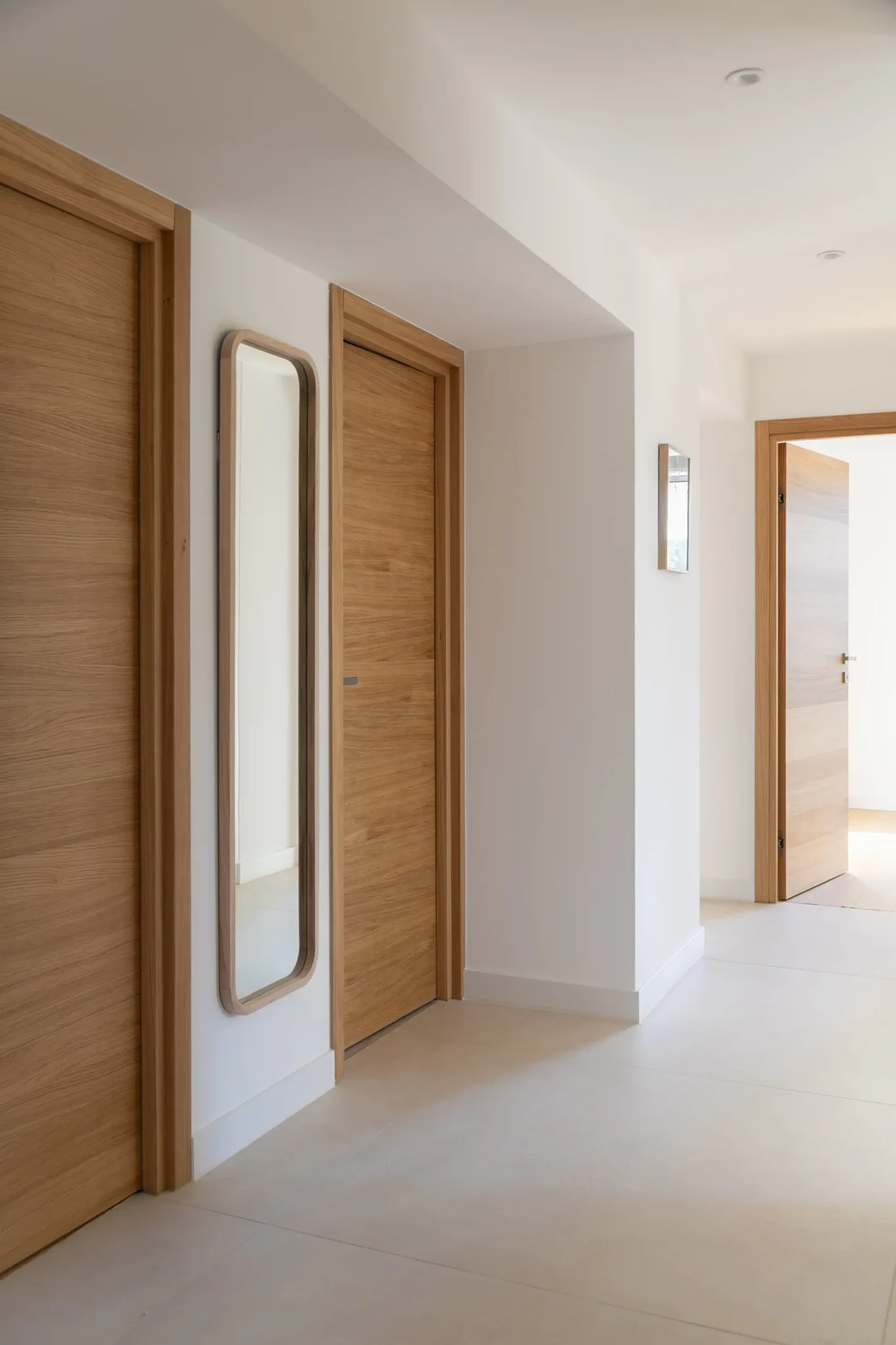 couloir avec portes en bois et bati de portes en bois sol en carrelage grand format effet béton ciré spot pladonf
