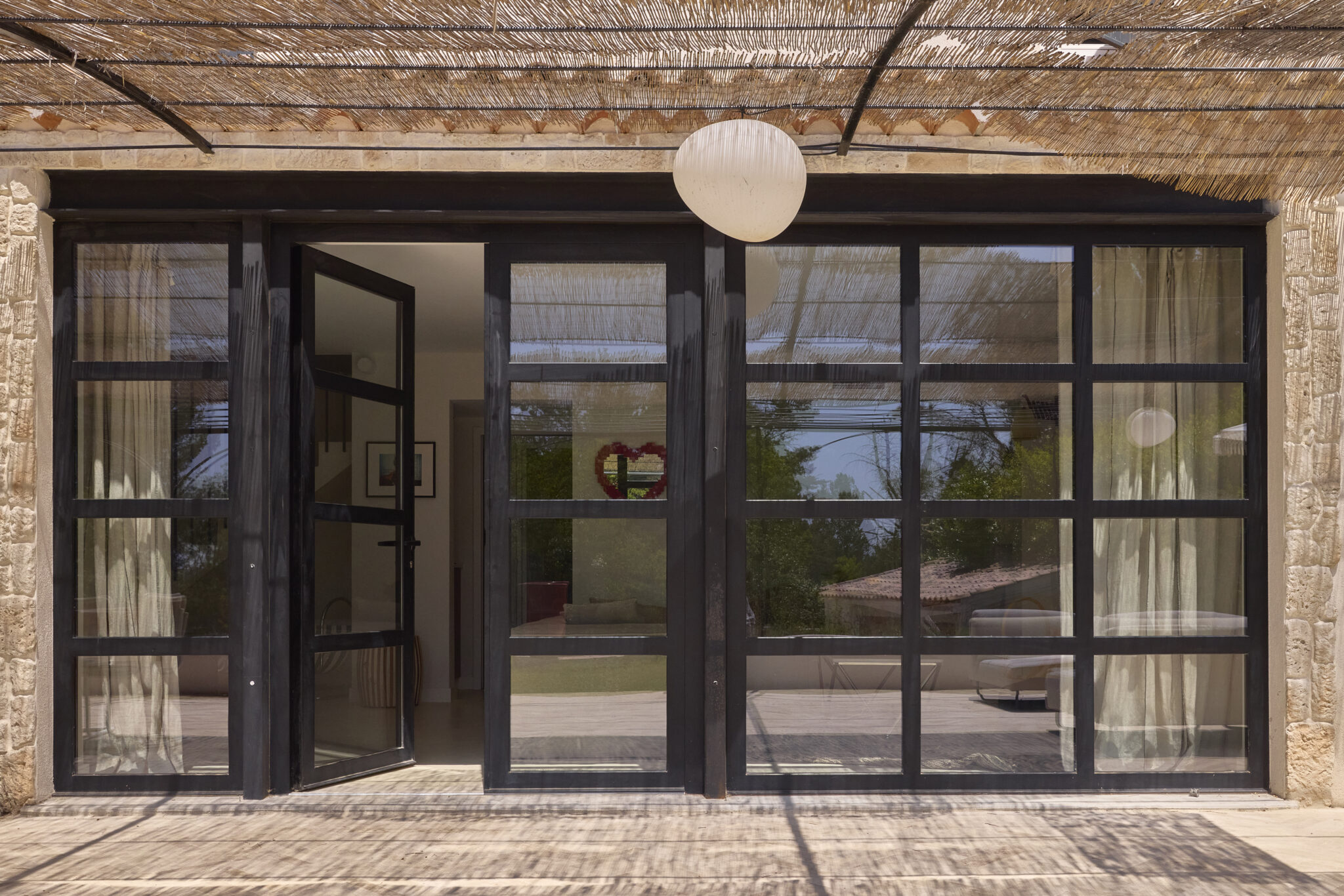grande baie vitrée salon ouverture mur porteur 5m delong avec IPN peint en noir encadrement de fenêtre en parement pierre pergola en fer forgé avec canisses