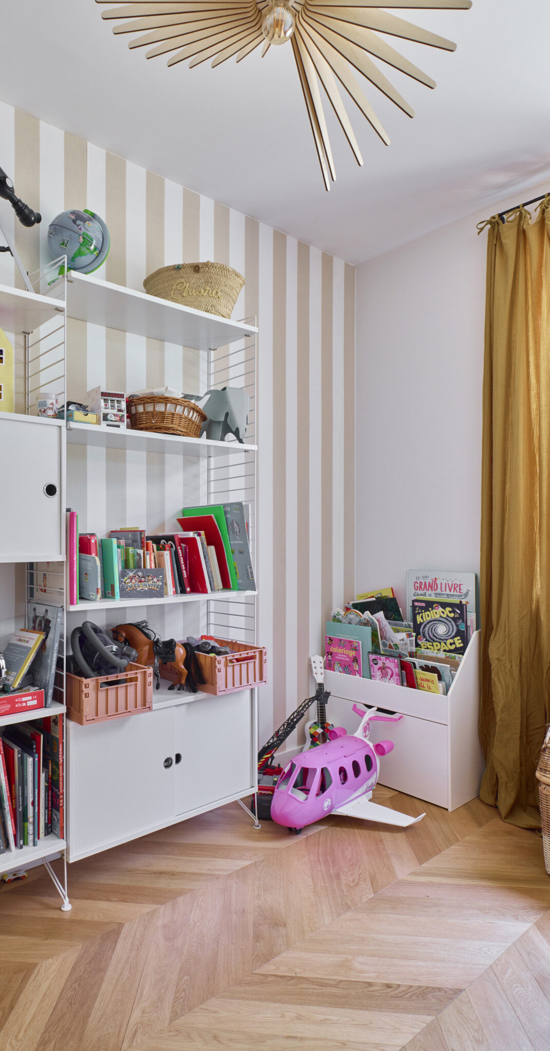 salle de jeux enfants avec parquet chêne en point de hongrie papier peint à rayures rideaux en lin ocre et suspension lumineuse atelier loupiotte