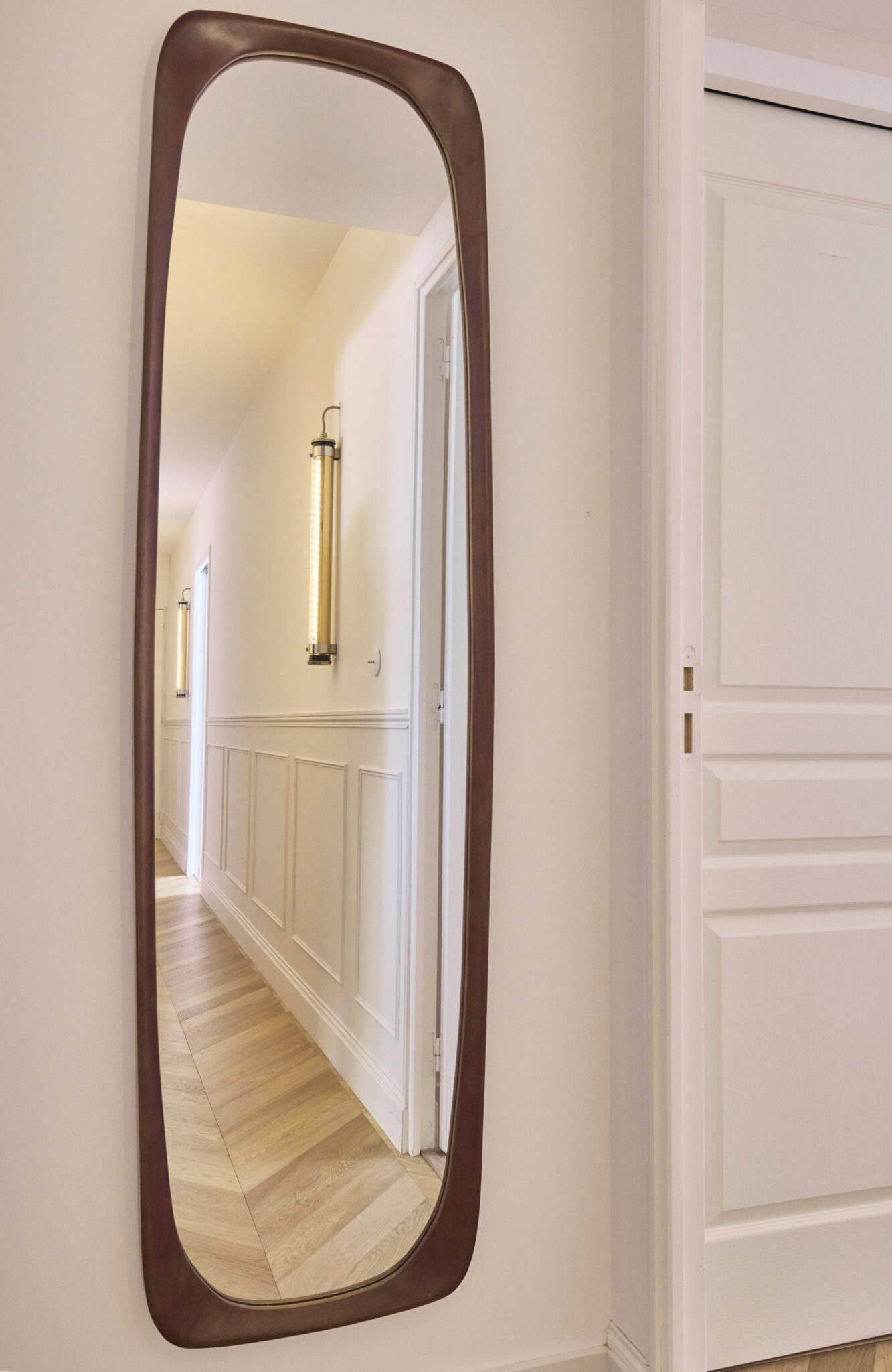 couloir en parquet chêne point de hongrie applique murale de chez Sammode studio modèle Elgar porte moulurée et soubassement de mur en moulures avec corniche style parisien